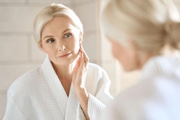 The SPF 30 Habit I Overlooked That Made Skincare Simple Woman looking at skin in the mirror.