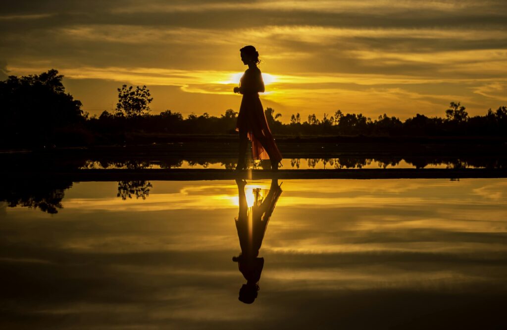 A serene silhouette of a woman during sunrise, reflecting perfectly on calm water.