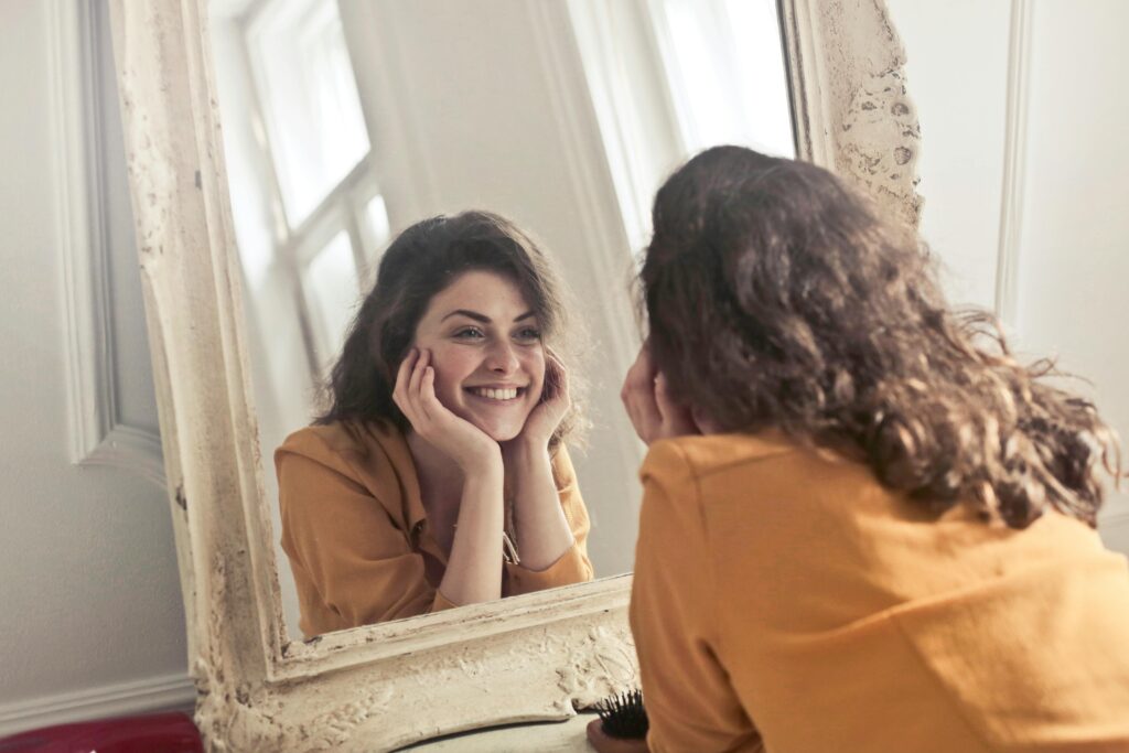 pexels-photo-774866-774866 - Beautiful by Suzie A cheerful woman smiles at her reflection in a vintage-style mirror, exuding positivity and warmth.